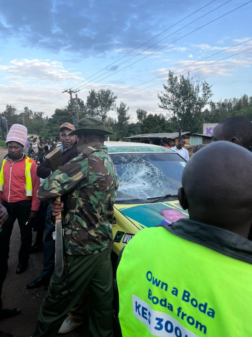 Damaged Nyakera car and a policeman holding a panga used by the goons