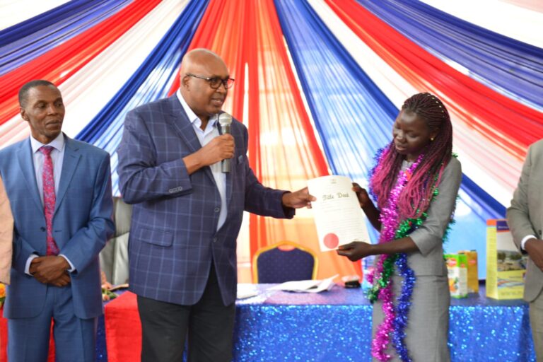 MKU founder Simon Gicharu hands over a title deed for a piece of land that he has bought to Milly Nafula