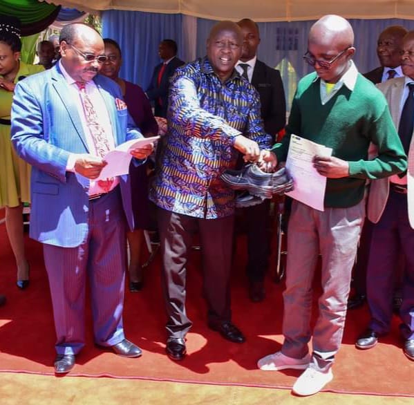 Nyeri County governor Mutahi Kahiga (centre) giving one of the beneficiaries a pair of shoes made by the County Government. Looking on is his deputy David Kinaniri Warui.