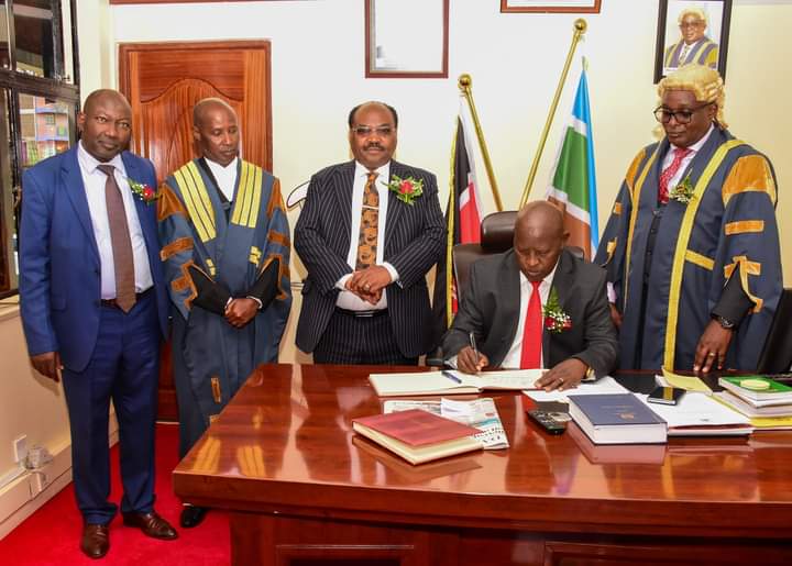 Nyeri County governor Mwalimu Mutahi Kahiga (seated) signing a visitors book at Nyeri County Assembly.