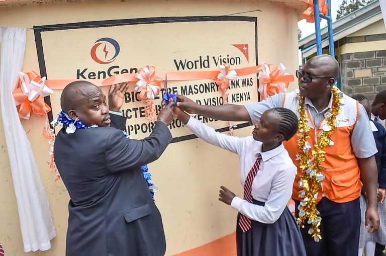 Eng. Clety Bore of KenGen (left) and Mr Fredrick Kasiku of World Vision (right) assisted by a pupil unveils a plaque during the commissioning.