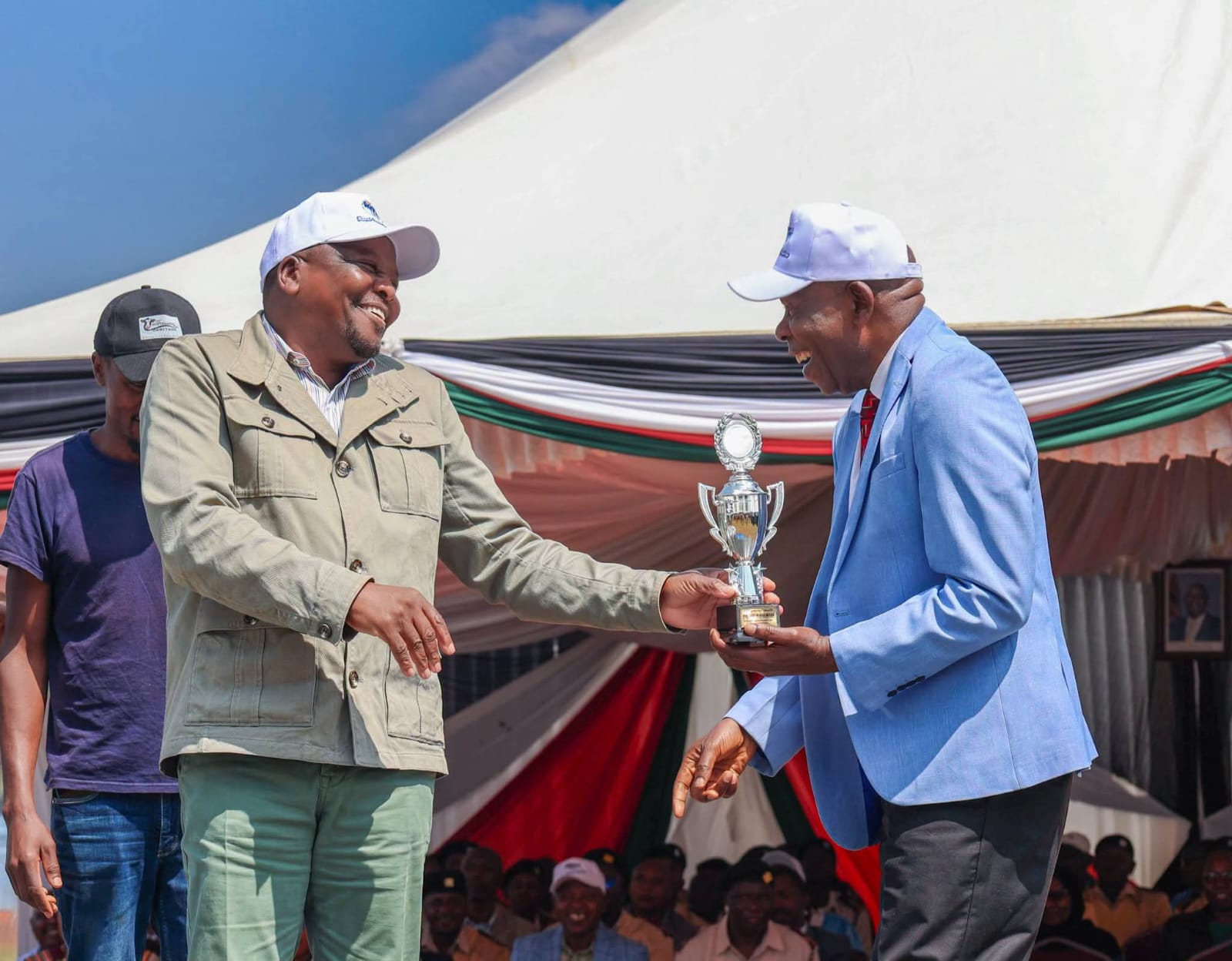 CS Mutahi Kagwe (left) handing over a trophy to Wakulima dairy chairman Muhika Mutahi.