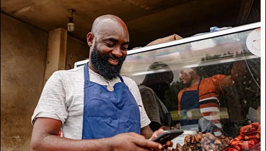A street vendor engages with his mobile phone, potentially managing digital transactions for his small business. This scene reflects the growing intersection of technology and informal economies.